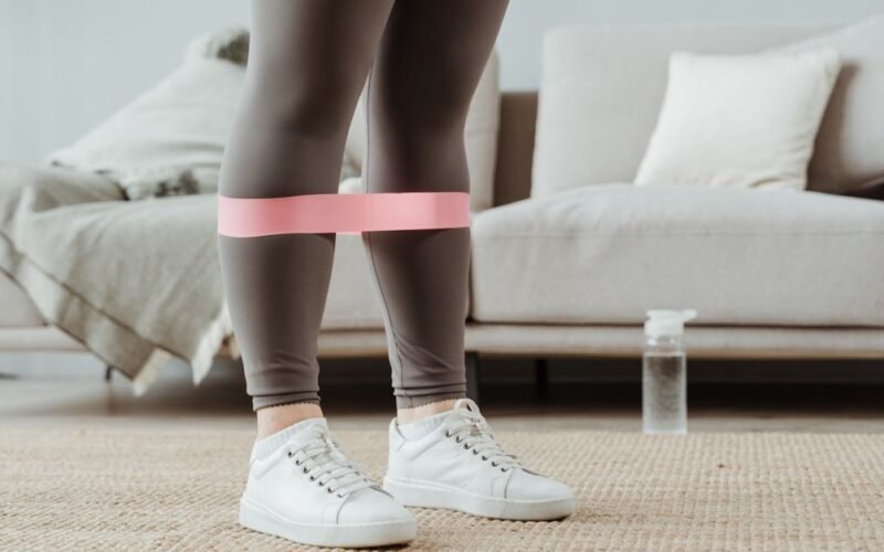 Woman using pink resistance band for leg exercises indoors
