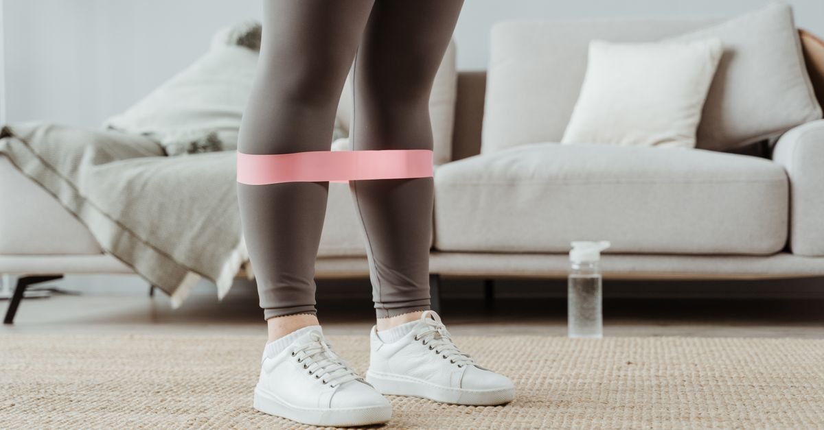 Woman using pink resistance band for leg exercises indoors