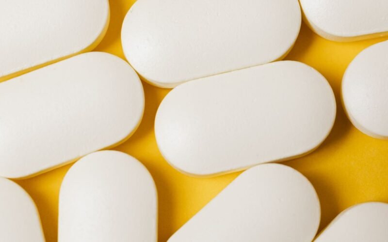 Close-up of white oval pills on a bright yellow surface