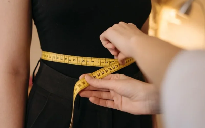 Hands wrapping a yellow tape measure around a person's waist