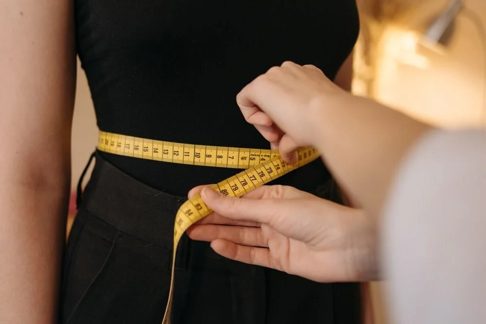 Hands wrapping a yellow tape measure around a person's waist